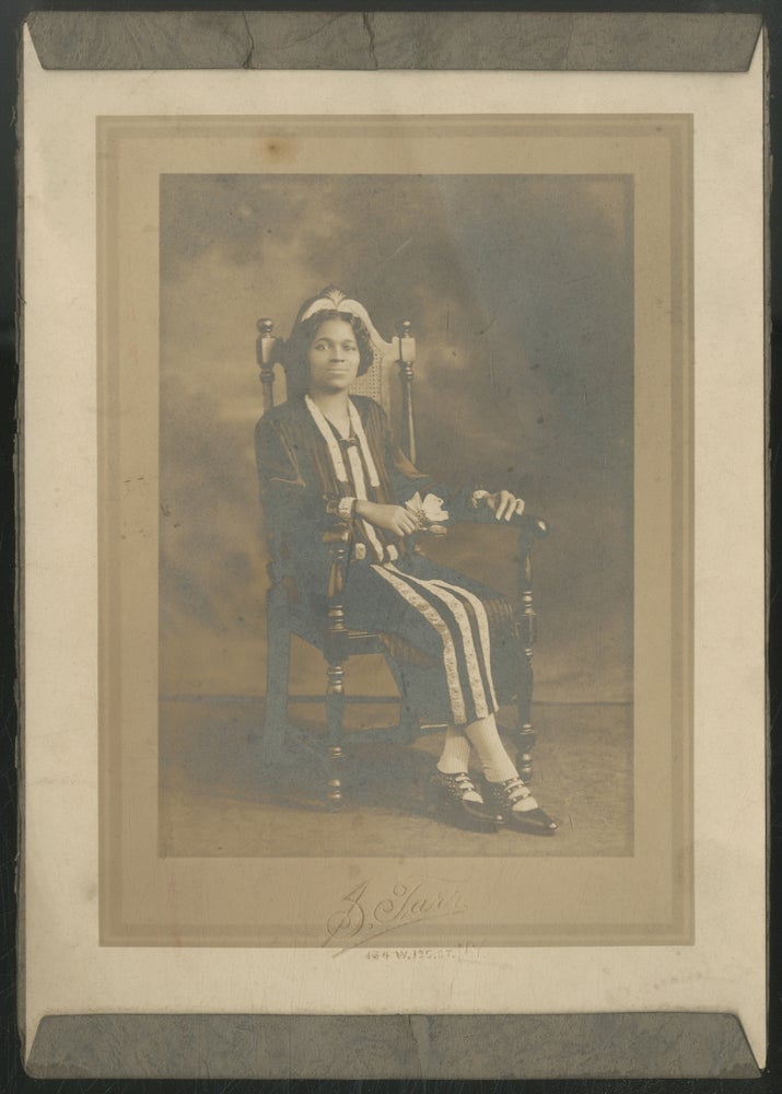 Item #443478 [Portrait photograph]: African-American Seated in a High-back Chair holding a Flower [circa 1905]